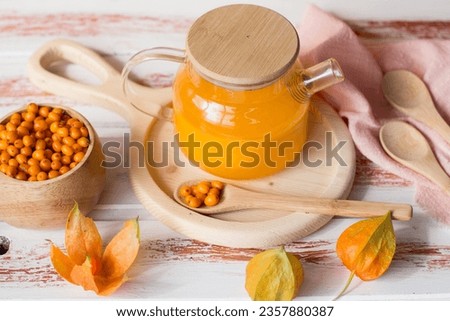 yellow tea with sea buckthorn berries in a glass teapot. Decorated with physalis and autumn pumpkins, dried herbs for winter in the background Royalty-Free Stock Photo #2357880387