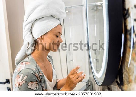 Smiling woman applies facial cream in her bathroom as part of her healthy morning routine.