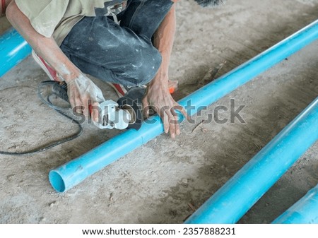 Plumper using electric grinder to cut pvc pipe without gloves in building site. Royalty-Free Stock Photo #2357888231