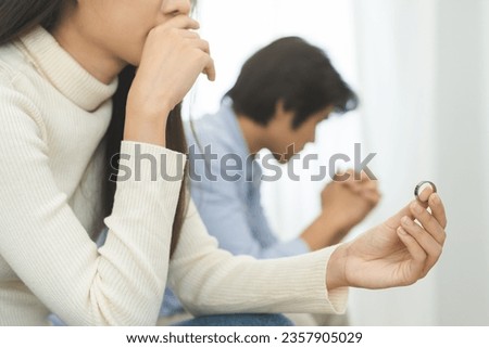 Stressed asian young couple man, woman quarrel on couch, relationship in trouble. Wife's hand holding wedding ring in disappointment and upset her husband, which may lead to divorce. Problem of family Royalty-Free Stock Photo #2357905029