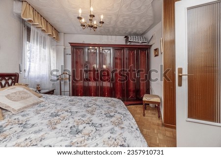 A vintage bedroom with a bed with a floral print bedspread and a large shiny mahogany wood wardrobe