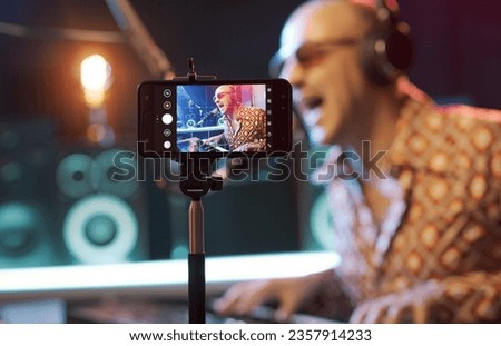 Artist recording a song in the studio and shooting a video using a smartphone