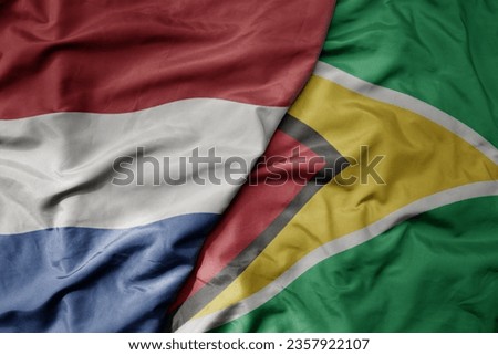 big waving national colorful flag of netherlands and national flag of guyana . macro