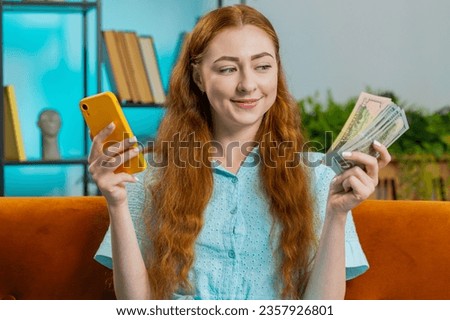 Planning family budget. Smiling young redhead woman counting money cash, use smartphone calculate domestic bills at home room. Girl satisfied of income and saves money for planned vacation, gifts Royalty-Free Stock Photo #2357926801