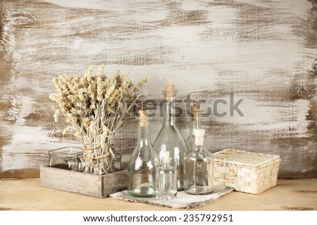 Glass bottles and dry flowers on rustic wooden background.