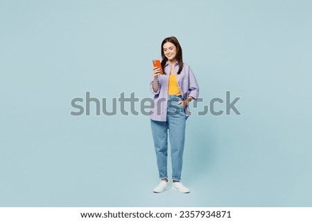 Full body young happy woman she wears purple shirt yellow t-shirt casual clothes hold in hand use mobile cell phone isolated on plain pastel light blue background studio portrait. Lifestyle concept