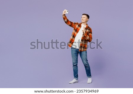Full body young man he wears checkered shirt white t-shirt casual clothes do selfie shot on mobile cell phone post photo on social network show v-sign isolated on plain pastel light purple background