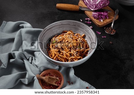 Udon wheat noodles stir-fried with chicken and vegetables. The side view, horizontal frame emphasizes the ingredients on a black background, with spices and a napkin.