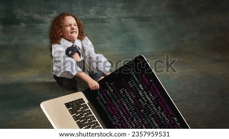 Beginner IT programmer. Emotional little girl with curly hair in vintage blouse pulls laptop over dark green background. Concept of creativity, comparison of eras, retro, vintage, kids fashion