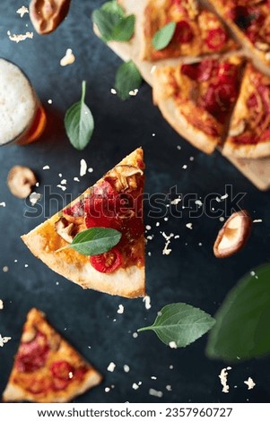 Top view picture of pizza slice falling towards the background. The ingredients are on different heights. There are basil, mushrooms, cheese. Glass of beer and rest of pizza on the background.
