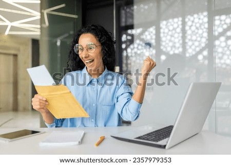 Successful and happy business woman at workplace received envelope mail fox, Hispanic woman joyfully celebrating good news from message notification inside office, woman winner holding hand up. Royalty-Free Stock Photo #2357979353