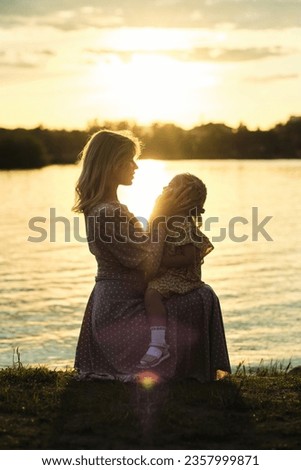 mom and her child hugging at sundown by lake epitomizes the rapeutic power of nature. warm hues of sunset symbolize mental solace that comes with close relationships and natural beauty.