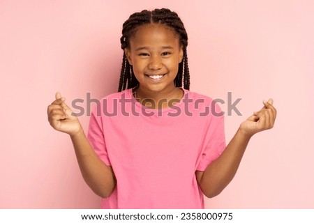 Positive African girl in pink t shirt gesturing showing heart from fingers, k pop culture, isolated on pink background, mockup. Young modern child with toothy smile looking at camera Royalty-Free Stock Photo #2358000975