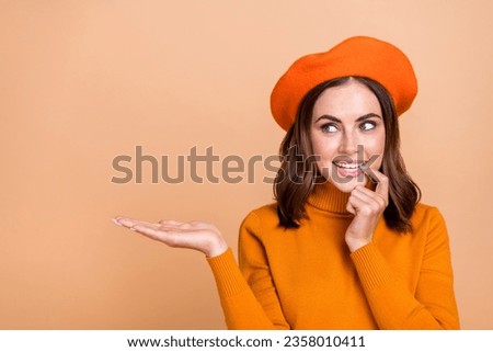 Photo of pretty mischief lady bite fingernail wear trendy orange clothes palm show empty space look ad isolated on beige color background
