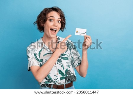 Photo of funky impressed lady wear print shirt pointing finger bank card empty space isolated blue color background