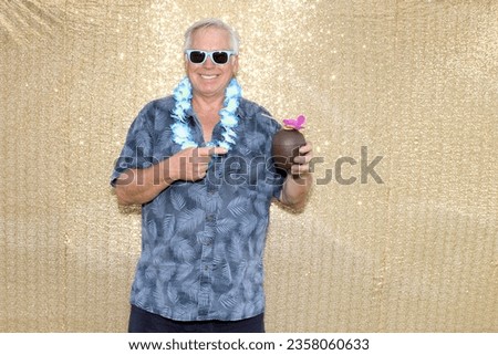 Hawaiian. Photo Booth. Maui Hawaii. A man smiles and holds up a Plastic Coconut Cup filled with Cocktails while having his picture taken in a Photo Booth. Photo Booths are Popular at Parties. 