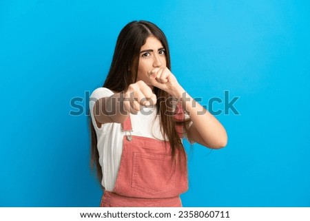 Young caucasian woman isolated on blue background with fighting gesture