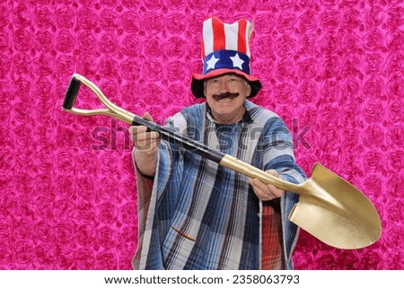 Golden Shovel. Photo Booth. A man wearing an American Flag Hat and Mexican Serape holds a Golden Shovel and smiles while he has his picture taken in a Photo Booth at a  party. Golden Shovels are cool.