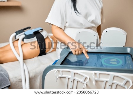 A female worker in a spa salon applies body sculpting equipment to her clients buttocks to enhance the clients body aesthetics.