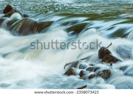 A stormy, turbulent river with a strong current. Streams of water wash large stones in the river. Clear water in a mountain river. Wet stones in the water close-up Royalty-Free Stock Photo #2358073423
