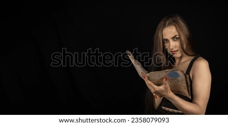 Copyspace. On a halloween night, a gothic woman is addicted to reading a book with black magic. A beautiful woman with long hair is holding a book with a text. Halloween and witchcraft concept.