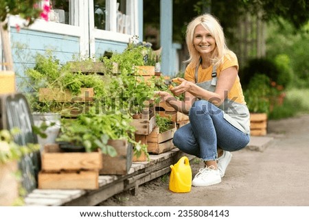 Smiling Mature Woman Taking Care About Plants In Crates At Her Backyard, Happy Beautiful Senior Lady Wearing Apron Enjoying Gardening And Eco Farming, Using Pruning Shears Secateurs, Free Space Royalty-Free Stock Photo #2358084143