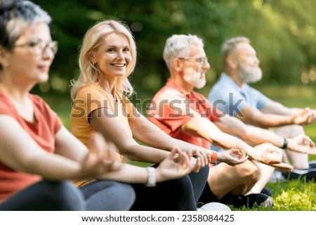 Beautiful Senior Woman Attending Group Yoga Class Outdoors, Happy Mature Female Practicing Meditation With Friends In Park, Sitting In Lotus Position And Smiling At Camera, Selective Focus Royalty-Free Stock Photo #2358084425