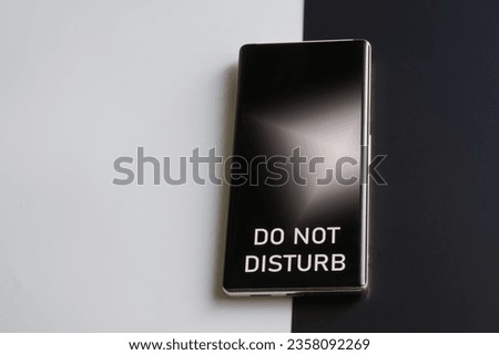 Smartphone with the inscription do not disturb on a two-tone black and white background. Concept of exhaustion, fatigue, depression, rest, solitude and introvertism. Close-up  Royalty-Free Stock Photo #2358092269