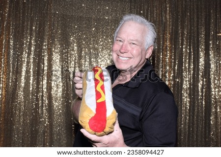 Photo Booth. Hotdog. A man smiles as he poses for his picture to be taken while he is in a Photo Booth with a Giant Hotdog with Mustard. People love Photo Booths for Parties and Events. Hotdogs. 