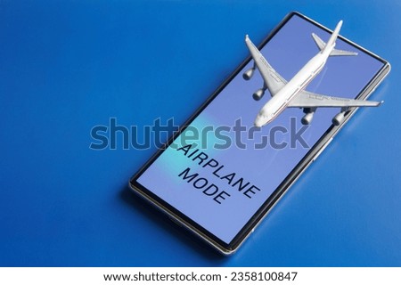 Mobile phone - smartphone with the inscription "Airplane mode" and toy passenger plane. Blue background. Disabling the communication functions of gadgets during an airplane flight. Photo. Close-up Royalty-Free Stock Photo #2358100847