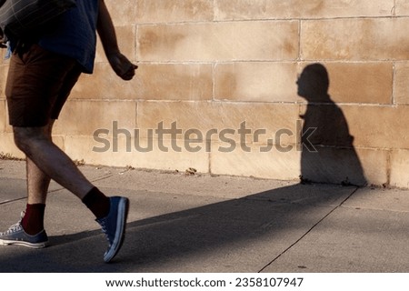 Man walking along a concrete wall with his shadow behind him