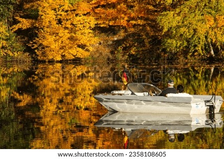 a motorboat and an autumn forest of red yellow and green autumn colors are reflected in the lake surface. 