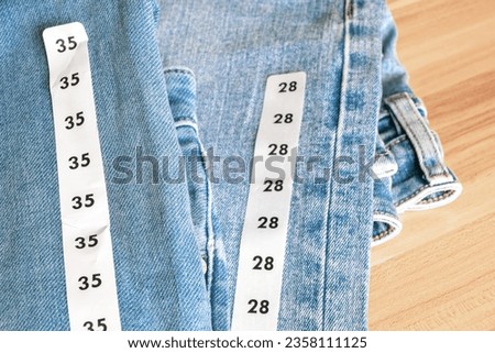 Close up shot of a couple's matching blue jeans of different sizes on wooden background.  Royalty-Free Stock Photo #2358111125