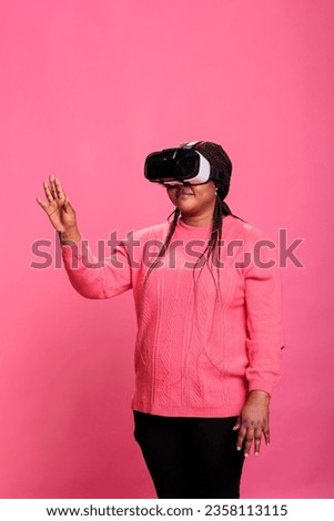 Joyful african american model playing virtual reality games using vr headset enjoying 3d experience in studio with pink background. Electronic futuristic experience with augmented tech innovation