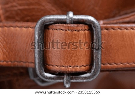 metal clasp on the strap of a brown leather bag. Close-up.