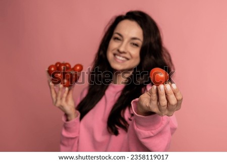 Waist-up portrait of a joyous brunette demonstrating fresh tomatoes in the glass bowl and her hand during the studio photo shoot. Healthy food choice concept