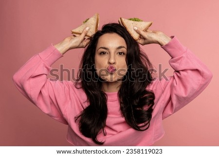Portrait of a funny lady making bunny ears using a couple of sarnies during the studio photo shoot. Fun and nutrition concept