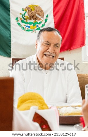 Mexican elderly man smiling during a family dinner celebrating mexican independence day. Grandfather laughing during a mexican traditional dinner celebrating national holidays in mexico.