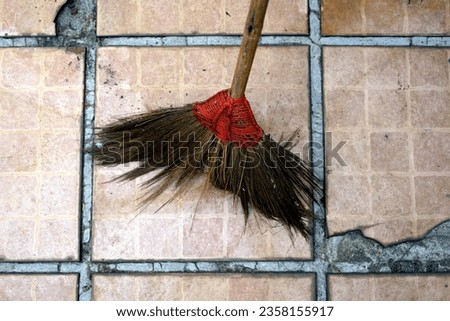 A old broom with red handle on the old tiles floor, closeup of photo