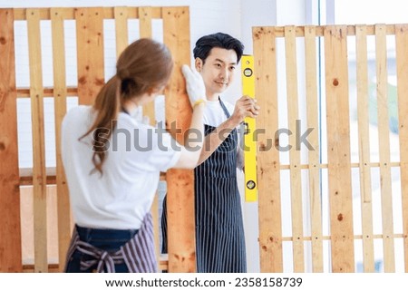 Asian professional male carpenter in apron holding using water level gauge measuring wood stick plank while female colleague writing short note on paper clipboard in home decoration building workshop. Royalty-Free Stock Photo #2358158739