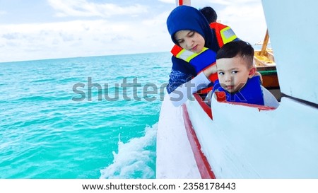 photo of mother and child on a wooden boat wearing life jackets looking towards the green sea, with bright blue sky and white clouds. copy space. Belitung Island - Indonesia