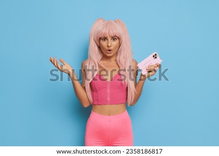 Surprised young woman in pink wig holding smartphone and looking at camera Royalty-Free Stock Photo #2358186817