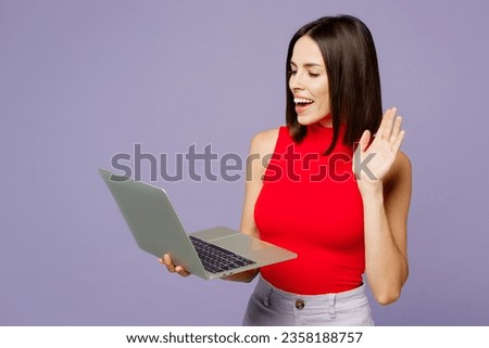 Young smiling happy cheerful IT woman she wears red tank shirt casual clothes hold use work on laptop pc computer waving hand isolated on plain pastel light purple background studio. Lifestyle concept