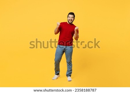 Full body young overjoyed happy Indian man wears red t-shirt casual clothes doing winner gesture celebrate clenching fists say yes isolated on plain yellow orange background studio. Lifestyle concept Royalty-Free Stock Photo #2358188787