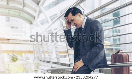business man wearing a suit is stressed from work stopped on a public walkway , He had a serious ,worried face because he was fired from his job the company he works for is about to go bankrupt Royalty-Free Stock Photo #2358204277