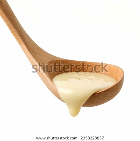 condensed milk in wooden ladle isolated on white background Royalty-Free Stock Photo #2358228837