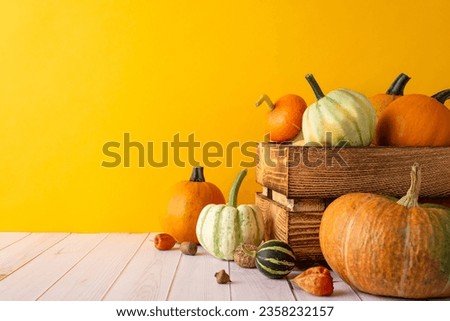 Autumn harvest theme with a side view image of a bountiful crop, featuring wooden crate box with pumpkins, pattypans, gourd, acorns and walnut on rustic wooden table against a warm, orange background Royalty-Free Stock Photo #2358232157