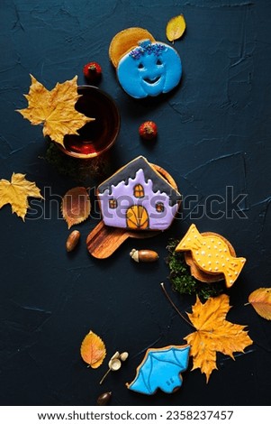 Autumn tea. Cup of tea, painted gingerbread, acorns and leaves on a black background.