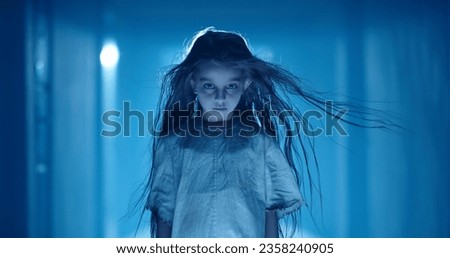 Little caucasian girl in ghost white sundress costume for halloween roaring into camera, frightening someone in hallway of haunted house 