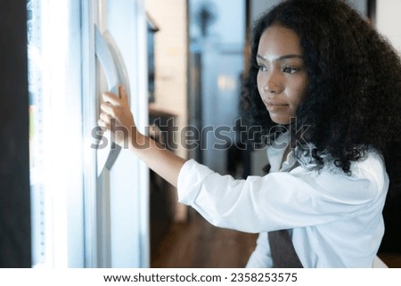 The owner of a coffee shop looks inside the refrigerator to retrieve chilled food to serve a customer.
